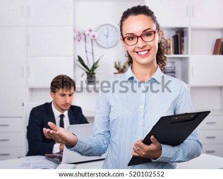 Glad smiling efficient business female secretary having cardboard in hands and working in office