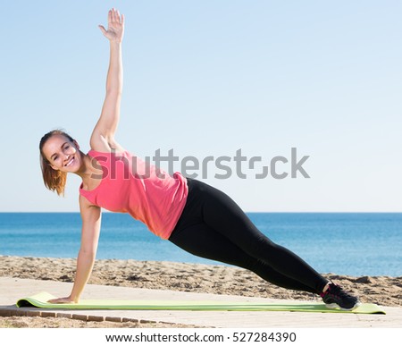 Charming girl exercising on exercise mat outdoor at the seaside