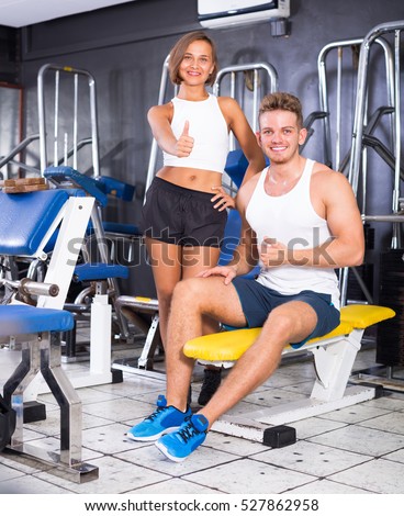 young joyful smiling man and woman fitness coaches taking break during workout in gym indoors. Focus on man