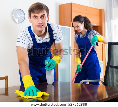 Young positive couple in uniform smiling and cleaning indoors