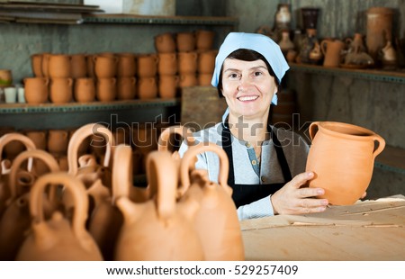 Happy mature female master among the finished products in the pottery workshop
