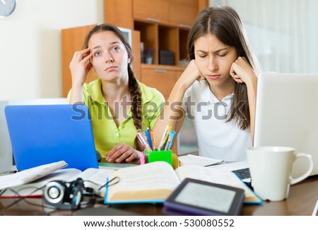 Dreary teenage student girls study in the home with a books and computers