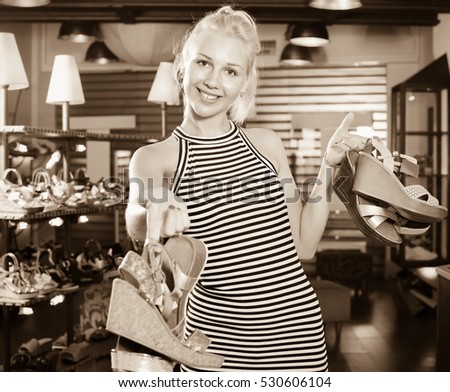 Happy beautiful  woman standing in boutique and having many shoes in hands