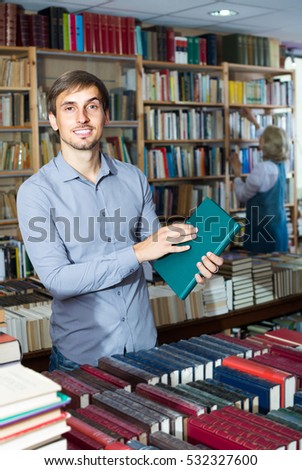 Young smiling  man holding book in hard cover in book store