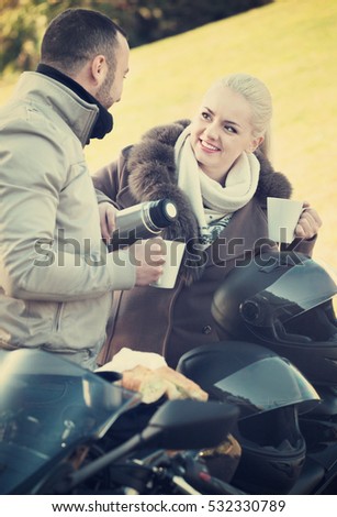 Positive smiling couple having picnic with coffee near cycle