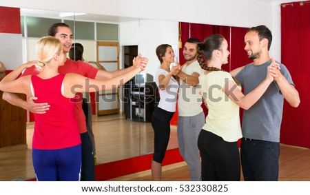 Young smiling people learning to dance waltz in pairs in dancing studio