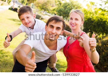 Glad parents with boy in school age having fun and showing thumbs up outdoors