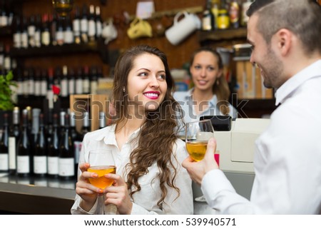 Smiling bartender and young guests couple with wine at bar counter. Focus on girl