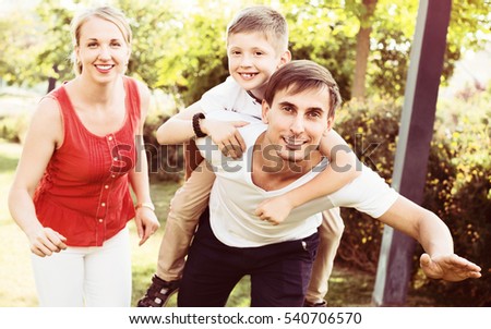 Portrait of cheerful family with boy sitting on father\'s back hugging each other in park
