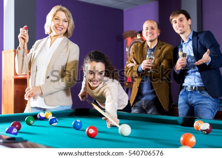 Attractive group of friends playing billiards and smiling in billiard club. Focus on the young woman
