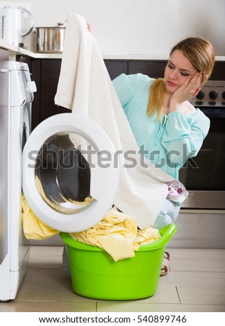 Unhappy housewife with dirty bed linen near washing machine