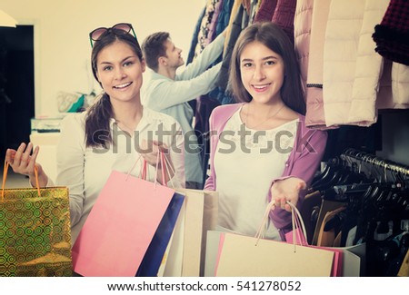 Guy and two shopaholic girls holding bags with clothes in apparel store