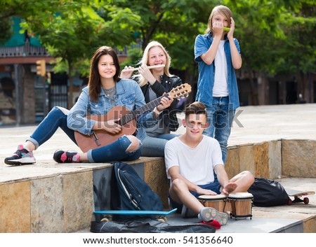 Glad girls and boys teenagers friends with musical instruments together outdoors
