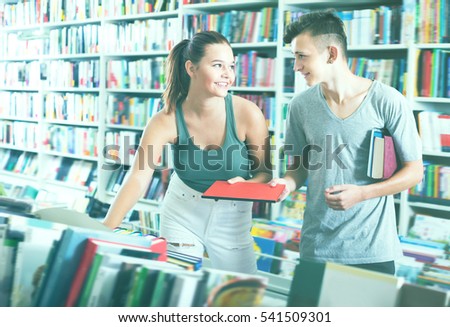 Portrait of positive teenage girl and boy taking new books together in shop