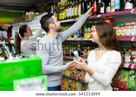 Happy customers in a liquor store. Woman holding a bottle of wine and looking at a man who is taking a bottle from a shelf