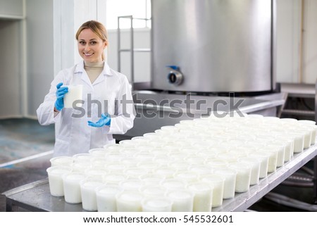 Smiling woman wearing uniform showing cottage cheese production process on dairy factory