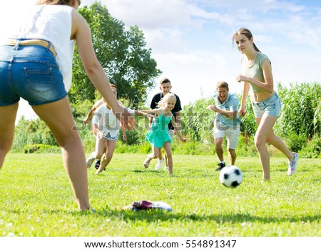 Happy parents with four kids playing soccer together on green field on summer day