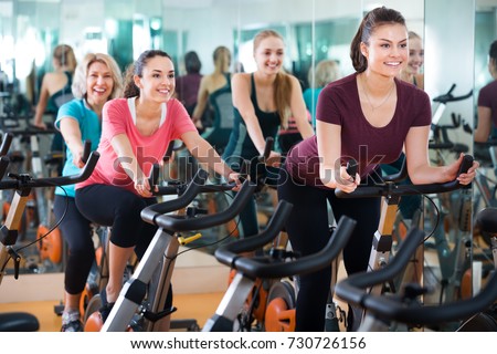 Positive females of different age training on exercise bikes together at modern fitness club