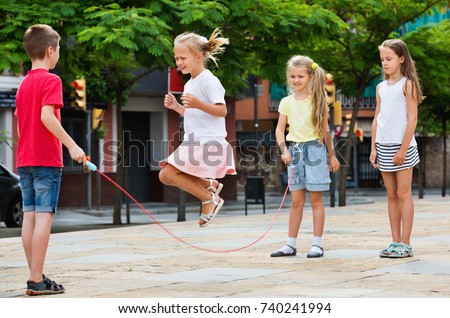 Happy kids in school age playing together with jumping rope outdoors