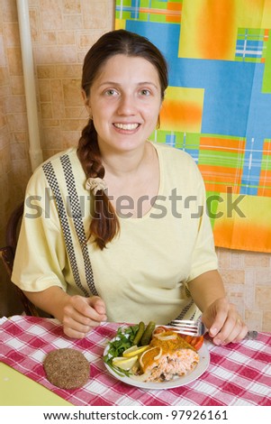 Young woman eating breaded fish in her kitchen