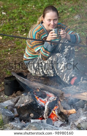 Female tourist drinking tea  at camp near fire