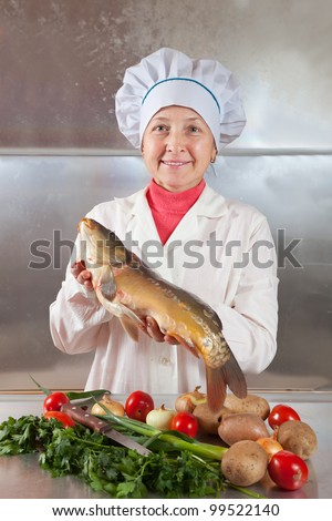 Cook woman with carp fish in her kitchen