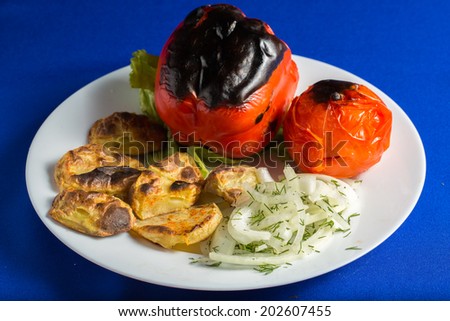 Roasted peppers with roasted potatoes and fresh onions on a white plate, isolated on blue background