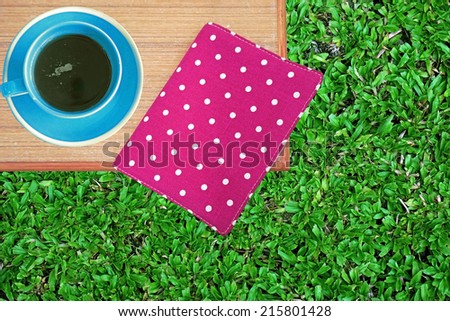 Pink book on table with coffee cup on green grass