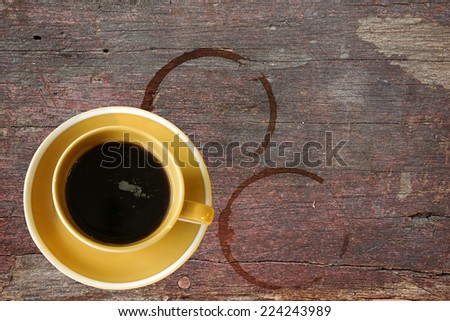Cup of hot black coffee on rough wooden table with stain rings