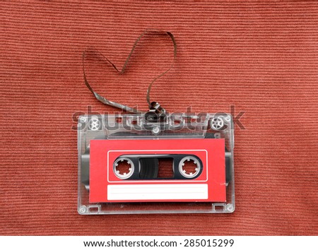 Vintage audio cassette with loose tape shaping a heart on red background