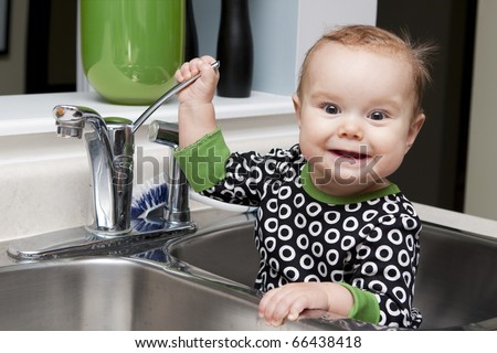 Baby sitting in kitchen sink playing with the tap