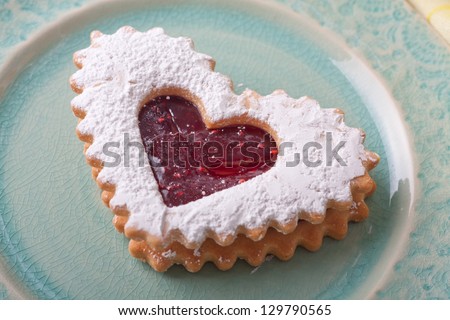 Heart sugar cookie with strawberry jam and confectioners sugar on a blue cracked glaze plate