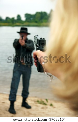 Rear view of woman pointing gun at man wearing cowboy hat, lake or river in background
