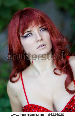 Portrait of a beautiful young woman in a long red wig with gothic makeup in the form of a vampire for Halloween