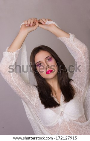 Studio emotional portrait of a beautiful young brunette woman with pink lips, wearing a white blouse