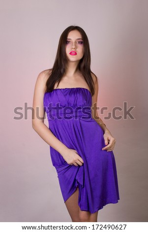 Emotional studio portrait of a beautiful brunette girl in a cocktail dress and lilac bright evening makeup with pink lips