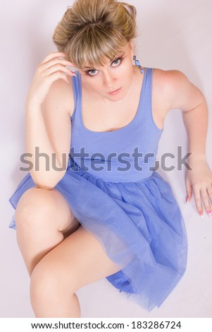 Portrait of a beautiful young blonde woman with short hair and dressed in a blue short dress. Girl posing with different emotions in the studio.