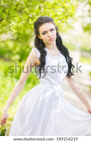 Beautiful young brunette posing in nature. Girl with hair and makeup in white romantic dress