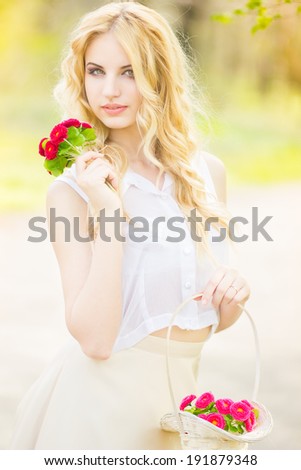 Portrait of a beautiful young blonde woman on a sunny summer day, strolling in the park. Woman in hands holds a basket of bright flowers