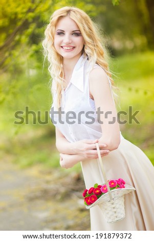 Portrait of a beautiful young blonde woman on a sunny summer day, strolling in the park. Woman in hands holds a basket of bright flowers