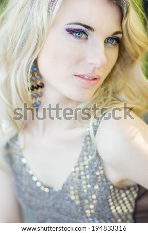 Portrait of a beautiful young blonde woman with long wavy hair in shiny black dress on nature.