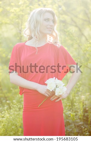 Portrait of a beautiful young blonde woman in the image of the bride. A girl wearing a red evening dress and in her hands she holds a bouquet of roses