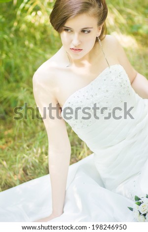 Portrait of a beautiful young bride in nature. Young woman holding a small bouquet of white roses in their hands