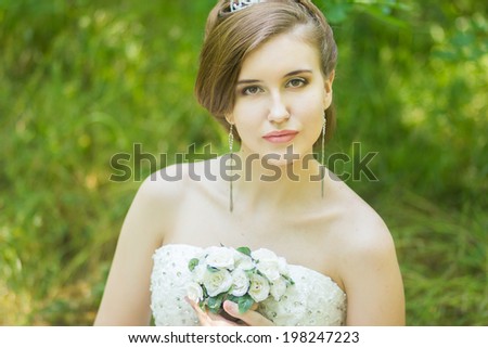 Portrait of a beautiful young bride in nature. Young woman holding a small bouquet of white roses in their hands