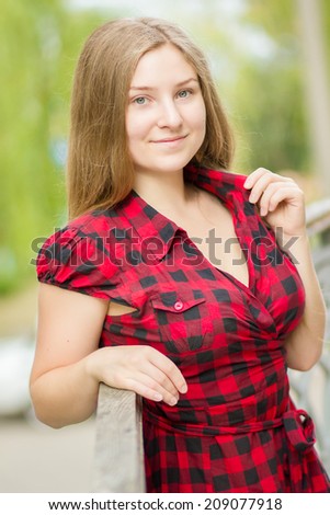 Portrait of a beautiful young woman with long brown straight hair. Girl posing in nature in a plaid dress on the balcony