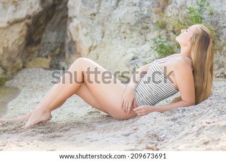 Portrait of a beautiful young blonde woman. Girl in a striped body to relax and rest in the summer on the beach near the water.