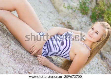 Portrait of a beautiful young blonde woman. Girl in a striped body to relax and rest in the summer on the beach near the water.