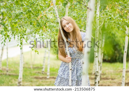 Portrait of a beautiful young woman with brown long hair on nature in a dress with a floral pattern. Girl resting in a birch forest