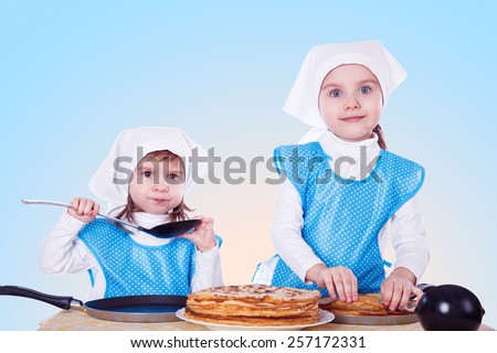Little children cooking pancakes. Two cute girls playing as chefs. Surprise for Mothers Day.  Blue background.
