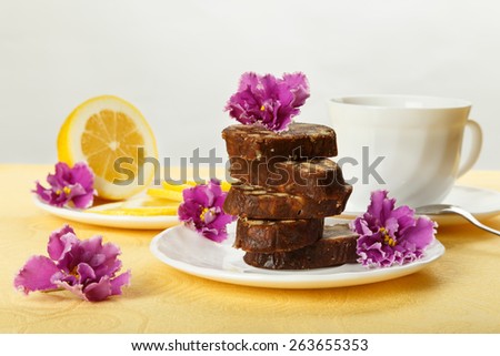Pile of delicious chocolate cake slices with the cookies filling, decorated violet flowers on a white plate with lemon and cup of tea.